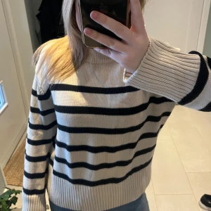 Randig stickad tröja - Snygg randig stickad tröja i beige och svart. Tröjan har långa ärmar och en ribbad krage. 