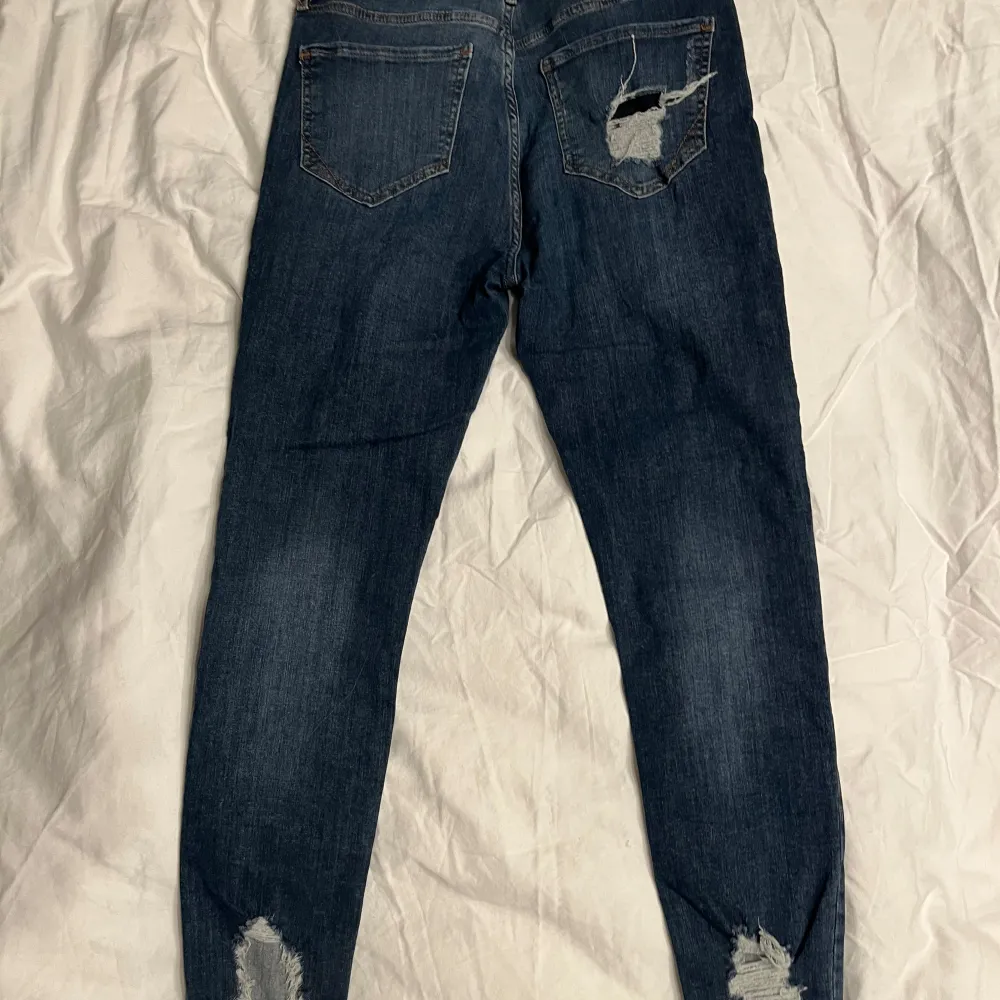 Säljer ett par mörkblå jeans från River Island i bra skick. De har en skinny passform och är dekorerade med slitningar för en trendig look. Perfekta för både vardag och fest!. Jeans & Byxor.