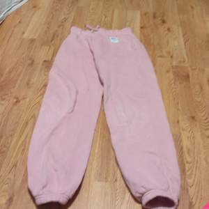 Supermysiga rosa mjukisbyxor i fleece. Perfekta för chilliga dagar hemma eller en avslappnad promenad. De har en elastisk midja med snörning och muddar vid bensluten för extra komfort. Ett måste för alla som älskar bekväma kläder!