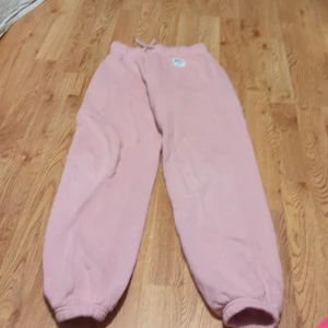 Rosa mjukisbyxor - Supermysiga rosa mjukisbyxor i fleece. Perfekta för chilliga dagar hemma eller en avslappnad promenad. De har en elastisk midja med snörning och muddar vid bensluten för extra komfort. Ett måste för alla som älskar bekväma kläder!