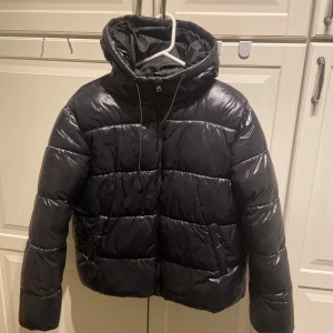 Svart pufferjacka med huva - Säljer denna snygga helt nya jackan, aldrig använd. Den är i storlek xs men är lite större i storleken men att ha typ en stickad tröja eller hoodie passa perfekt under