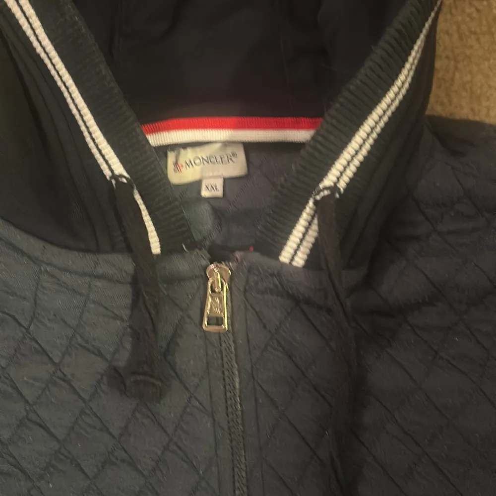 Säljer en snygg mörkblå quiltad jacka från Moncler i storlek XL. Jackan har dragkedja och långa ärmar med Moncler-logga på ärmen. Den har en sportig look med randiga detaljer vid krage och ärmslut. Perfekt för höst och vår!. Jackor.