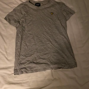 Grå t-shirt från Lyle & Scott - Säljer en grå t-shirt från Lyle & Scott i juniorstorlek 12/13. Den har en liten gul logga på bröstet och är i bomull. Perfekt för vardagsbruk och passar till allt! Skön och enkel stil för alla tillfällen. 
