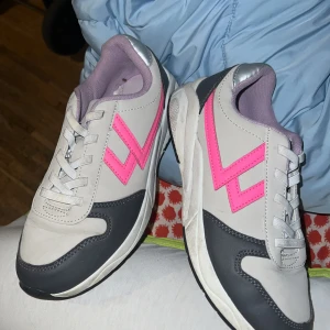 Grå och vita sneakers med rosa detaljer - Säljer ett par snygga sneakers i grått och vitt med coola rosa detaljer. Skorna har snörning och en bekväm passform, perfekta för vardagsbruk. De är i bra skick och storlek 35. Passar perfekt för en sportig look eller en avslappnad dag ute.