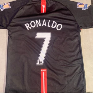 Svart Manchester United tröja med Ronaldo 7 storlek xs passar dig som är 165-170 - Säljer en svart Manchester United tröja med Ronaldo 7 på ryggen. Tröjan är från Nike och har AIG som sponsor på framsidan. Den har korta ärmar och är i Dri-FIT material för bra komfort. Perfekt för samlare eller fans av Ronaldo och United, Stolek mässigt skulle jag säga att om du är 165-170 så passar tröjan klockrent, jag knappt använt den eftersom är för liten!