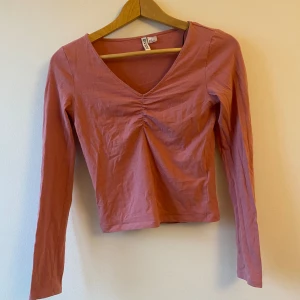 Rosa långärmad topp - Säljer en söt rosa långärmad topp i storlek S. Toppen har en v-ringad design med rynkdetalj framtill som ger en fin form.