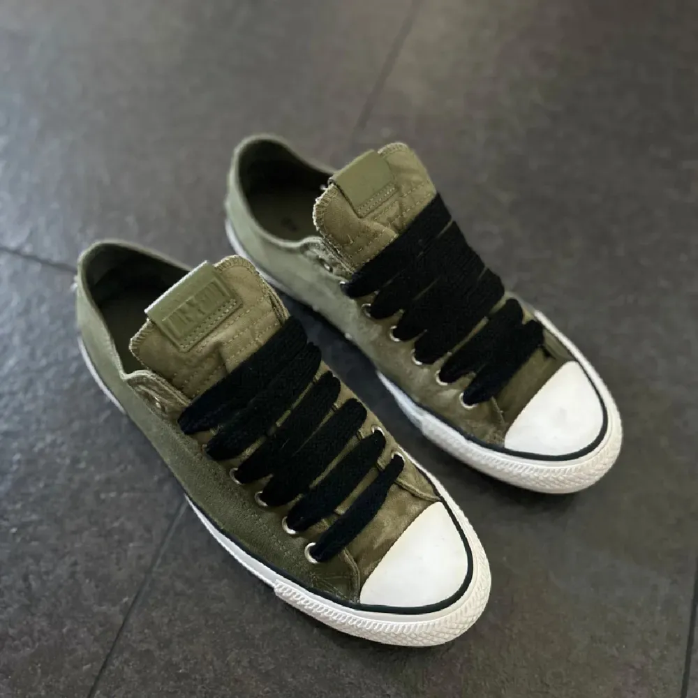 Säljer ett par olivgröna Converse sneakers i bra skick. De har en klassisk design med svart snörning och vit tåhätta. Perfekta för vardagsbruk och ger en avslappnad stil. Passar bra till både jeans och shorts!. Skor.