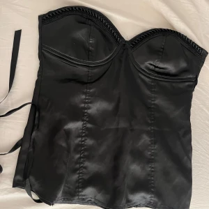 Svart korsett med snörning - Snygg svart korsett i satin med snörning bak. Den har en elegant design med vadderade kupor och dekorativa kanter. 💕💕 passar xs - s
