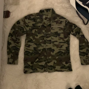 Camo Overshirt - Helt ny utan någon användning. Kommer ej ihåg vart jag köpte den men de va typ 999kr. Passar mig som är S. PASSAR PERFEKT T VÅRA CAMO CONVERSE