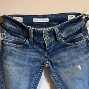 Säljer ett par snygga blå jeans från Pepe Jeans i modellen Venus. De har en straight fit och är lågmidjade, vilket ger en avslappnad look. Jeansen är i ett klassiskt blått denimtyg med en lätt tvättad effekt. Perfekta för vardagsbruk! Nypris: 999 kr 