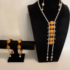 Snyggt smyckeset med halsband, armband och örhängen i orange och silver. Halsbandet har stora orange pärlor och silverkedja, medan armbandet matchar med liknande design. Örhängena har både orange och silverdetaljer. Perfekt för att liva upp en outfit! Ett par örhängen och ett par armband plus en halsband handgjorda mycket mycket fint nytt oanvänd 