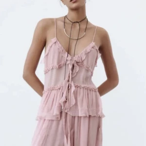 Rosa volanglinnetopp - Säljer en superfin rosa linnetopp med volangdetaljer och smala axelband. Toppen har en luftig och romantisk stil, perfekt för sommardagar eller en festlig kväll. Den är lätt och bekväm att bära, med en söt knytning framtill.