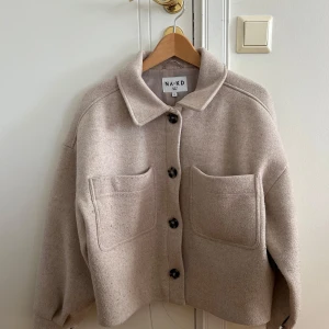 Beige kappa från NA-KD - Säljer en superfin beige jacka från NA-KD i storlek 34. Den har en oversized passform med stora fickor fram och knappar hela vägen. Perfekt för höst och vår! 🧥✨