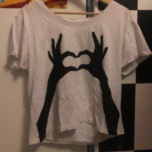 Vit t-shirt med tryck från Monki - Jag säljer en vit tröja med ett par händer som formar ett hjärta på framsidan. Tröjan är secondhand men har inga tecken på användning men det finns en lös söm. Den har storlek medium och är från monki