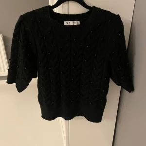 Svart stickad tröja från Zara - Säljer en snygg svart stickad tröja från Zara. Den har korta ärmar och ett fint mönster med små pärlor. Perfekt för både vardag och fest! 🖤det är Stl m men den sitter som xs/s