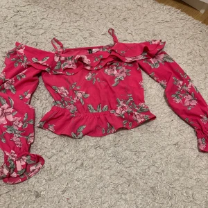 Rosa blommig offshoulder topp från H&M - Säljer en superfin rosa offshoulder topp från H&M med blommigt mönster. Toppen har långa ärmar och volangdetaljer vid axlarna och midjan. Perfekt för sommarens fester eller en dag på stan.