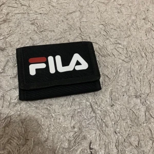 Fila plånbok - Säljer en svart plånbok från Fila i mycket bra skick. Den har flera fack för kort och en dragkedja på baksidan för mynt. Perfekt för att hålla ordning på dina grejer!