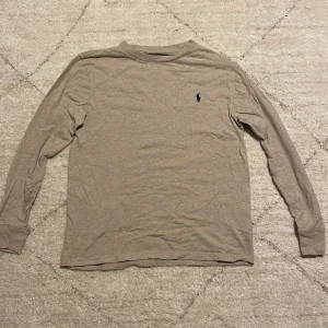 Beige långärmad tröja från Ralph Lauren - Säljer en stilren beige långärmad tröja från Ralph Lauren. Den har en liten broderad logga på bröstet och är perfekt för både vardag och lite finare tillfällen. Tröjan är i bra skick och passar perfekt till höst och vår. Skön och enkel att matcha med andra plagg!