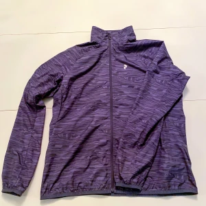 Unik Peak Performance Windbreaker - Säljer en snygg mörklila vindjacka med ett unikt mönster. Jackan har dragkedja och är perfekt för höst och vår. Den är långärmad och gjord i ett lätt syntetmaterial, vilket gör den idealisk för träning eller vardagsbruk. Passformen är normal och den har en diskret logga på bröstet. Han på bilden är 177cm och väger 65Kg skriv vid frågor👍