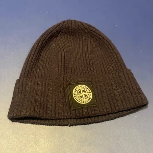 Svart ribbad mössa från Stone Island Nypris 1999 - Säljer en snygg svart ribbad mössa från Stone Island. Den är i mycket bra skick och perfekt för höst och vinter. Mössan har en broderad logga framtill och är gjord i ett mjukt material som håller dig varm. Passar perfekt till både vardag och fest! Öppen till prisförslag! 