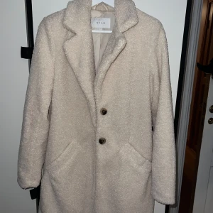 Beige teddyjacka från Vila - Mysig beige teddyjacka från Vila i storlek 36. Perfekt för höst och vinter med sin varma och fluffiga design. Jackan har långa ärmar och stängs med knappar framtill. Den har en klassisk krage och två fickor för extra bekvämlighet. Superfin och trendig för kyliga dagar! 🧥✨Använd 2-3 ggr max.