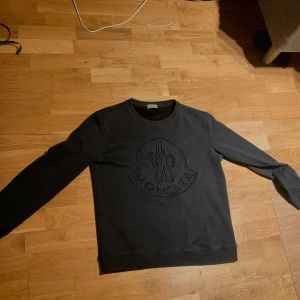 Svart tröja från Moncler - Säljer en snygg svart tröja från Moncler i mycket bra skick. Den har en stor Moncler-logga på framsidan och är perfekt för både vardag och lite finare tillfällen. Tröjan är gjord i ett mjukt material som känns skönt mot huden. Passar perfekt till höst och vinter! Tröjan är i storlek 1 vilket motsvarar S men passar även M. Ny pris på tröjan är 4699 kronor:)