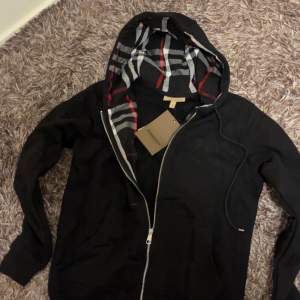 Säljer nu en oanvänd riktigt fin och stilig burberry zip hoodie som kommer att hålla dig varm under kalla dagar tack vore dess tjocka material. Hoodien är i nyskick och har aldrig används. INTE äkta