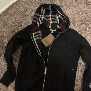 Burberry zip hoodie - Säljer nu en oanvänd riktigt fin och stilig burberry zip hoodie som kommer att hålla dig varm under kalla dagar tack vore dess tjocka material. Hoodien är i nyskick och har aldrig används. INTE äkta