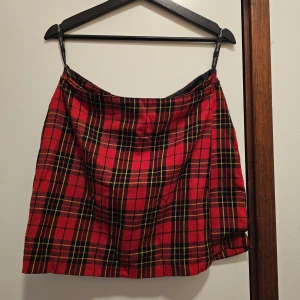 Rutig kjol från Impuls - Säljer en superfin rutig kjol från Impuls i storlek M. Den har ett klassiskt rött och svart rutmönster med inslag av gult. Perfekt för höst och vinter, och funkar lika bra till vardags som till fest. Kjolen är fodrad och har en omlott-design som ger en snygg look. 🖤❤️ 