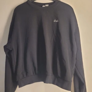 Svart sweatshirt från H&M - Säljer en svart sweatshirt från H&M i storlek XL. Den har en enkel design med texten 'Smile' broderad på bröstet. Perfekt för en avslappnad stil och passar till alla tillfällen. Tröjan är i bra skick och redo för en ny ägare!