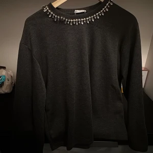 Svart tröja med pärldetaljer från Zara - Säljer en elegant svart tröja från Zara i storlek S. Den har långa ärmar och är dekorerad med glittrande pärlor runt halsringningen, vilket ger en lyxig touch. Perfekt för höst och vinter, både till vardags och fest. 🖤✨Aldrig använt 