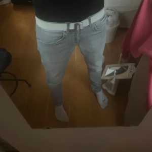 J.Lindeberg bälte - J.Lindeberg bälte i färgen vit med deras symbol i silver färg. Riktigt snyggt bälte. Har storlek W32 i jeans ungefär o denna passar perfekt vet inte direkta storleken i cm men antar ca 100cm.