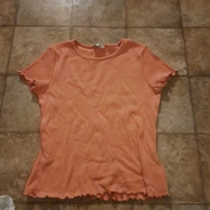 Orange ribbad topp - Säljer en söt orange ribbad topp i bra skick. Den har korta ärmar och en vågig kant vid ärmslut och nederkant. Perfekt för sommardagar eller som ett lager under en jacka. Passar både till vardags och lite mer avslappnade tillfällen. 🧡