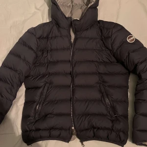 Svart dunjacka från Colmar - Säljer en snygg svart dunjacka från Colmar i mycket bra skick. Jackan har en dragkedja framtill och en huva för extra värme. Perfekt för kalla vinterdagar och har en stilren design som passar till det mesta. Storleken är dam s men sitter som xs och den är superbekväm att ha på sig.