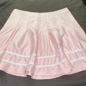 Rosa kjol med vita detaljer - Superfin rosa kjol med vita ränder som ger en söt och lekfull look. Kjolen har en A-linjeformad design som ger en härlig volym och rörelse. Perfekt för vår och sommar, och kan enkelt matchas med en enkel topp för en chic outfit. 🩷