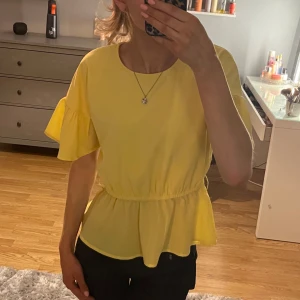 Gul blus med volangdetaljer - Säljer en superfin gul blus med volangdetaljer på ärmarna. Perfekt för sommardagar eller en festlig kväll. Blusen har en lös passform och är tillverkad i ett lätt och luftigt material. Den har korta ärmar och en elastisk midja som ger en smickrande siluett. Har varit ett band till men har tyvärr tappat bort de❤️