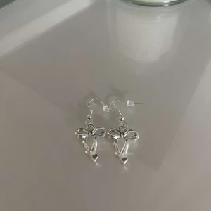 Silverfärgade örhängen med ängeldesign - Säljer ett par superfina silverfärgade örhängen med en söt ängeldesign. De är perfekta för att ge en extra touch till din outfit, oavsett om det är till vardags eller fest. Örhängena har en krok för enkel användning.