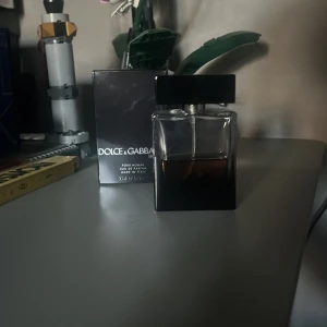 Dolce & Gabbana Pour Homme Eau de Toilette - Säljer en elegant och stilren parfymflaska från Dolce & Gabbana. Flaskan är fyrkantig med en mörk tonad glasdesign och ett svart lock. Perfekt för den som vill ha en klassisk och maskulin doft. Flaskan är 125 ml och kommer i sin originalförpackning.