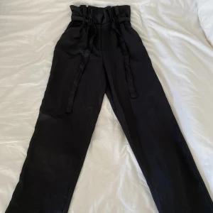 Kostymbyxor  - Svart kostymbyxa med snörning samt dragkedja i midjan. Använd vid ett tillfälle.