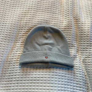 Grå mössa från GANT - Säljer en stilren och bekväm grå mössa från GANT. Den är ribbad och har en liten logga framtill. Perfekt för kyliga dagar och passar till det mesta i garderoben.