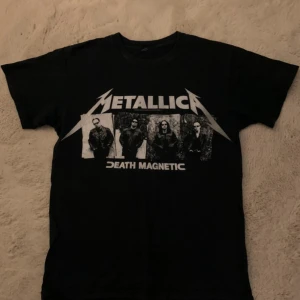 Svart Metallica T-shirt - Cool svart T-shirt med Metallica 'Death Magnetic' tryck på framsidan och 'World Magnetic Tour' motiv på baksidan. Perfekt för fans av bandet som vill visa sin kärlek till musiken.