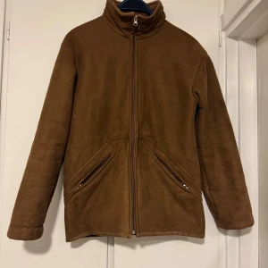 Brun fleecejacka med dragkedja - Säljer en brun fleecejacka med dragkedja och hög krage. Jackan har två fickor med dragkedjor framtill och är perfekt för kyligare dagar. Den är långärmad och har en enkel design som passar till det mesta.