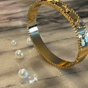 Guldfärgat armband i rostfritt stål  - Elegant guldfärgat armband med detaljerade blommönster i rostfritt stål. . Perfekt för att lägga till en touch av glamour till din outfit.