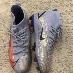 Nike fotbollsskor i ljusblått och silver - Snygga Nike fotbollsskor i ljusblått med silverdetaljer och svarta logotyper. Storlek 38 men är mindre i storlek. 