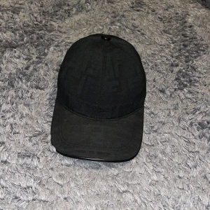 Svart keps från Fendi - Snygg svart keps från Fendi med diskret mönster och justerbart spänne baktill. Perfekt för en stilren look.