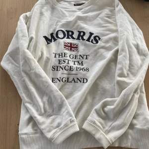 Vit sweatshirt från Morris - Säljer en vit sweatshirt från Morris med tryck framtill. Tröjan har långa ärmar och ribbade muddar vid ärmslut och nederkant. Perfekt för en avslappnad stil. 🏷️ lite missfärgat på vissa ställen men syns inte jätte tydligt, går säkert att få bort med tvätt