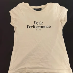 Vit t-shirt från Peak Performance - hej! säljer en vit t-shirt från Peak Performance med tryck 'Peak Performance T-shirten har korta ärmar och en rund halsringning. Perfekt för en avslappnad stil💞