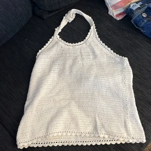 Vit virkad linne - Säljer en söt vit virkad linne med halterneck-design. Toppen har fina virkade detaljer längs kanterna och är perfekt för varma sommardagar. Passar bra till både jeans och kjol. Perfekt för en avslappnad och stilren look.