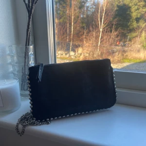 Svart kuvertväska med kedjedetaljer - Snygg svart kuvertväska från Zara med kedjedetaljer längs kanterna. Väskan har flera fack och en dragkedja för säker förvaring. 