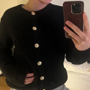 Svart kofta med dekorativa knappar - Säljer en svart kofta med dekorativa knappar i guld. Koftan har en rund halsringning och långa ärmar. Aldrig använt💕